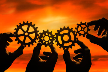 Gears in the hands of people against the sunset, the evening sky. the mechanism of teamwork.