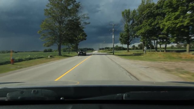 Driving towards storm in rural area. Sun still out with dramatic lighting. Approaching traffic at beginning. 