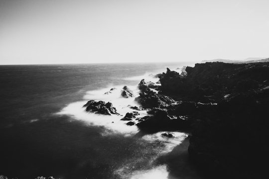 Black and white image of a seascape with mountains and rocks, long exposure and waves that become foam. Image for black and white backgrounds. Tenerife island wallpaper