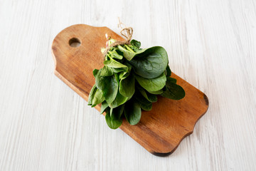 Fresh raw spinach on rustic wooden board on a white wooden background, low angle view. Close-up.