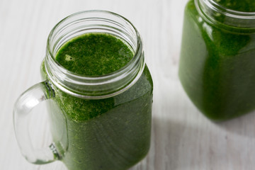 Green smoothie with avocado, spinach and banana in glass jars over white wooden background, low angle view. Closeup.