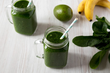 Green smoothie with avocado, spinach and banana in glass jars over white wooden surface, side view. Close-up.