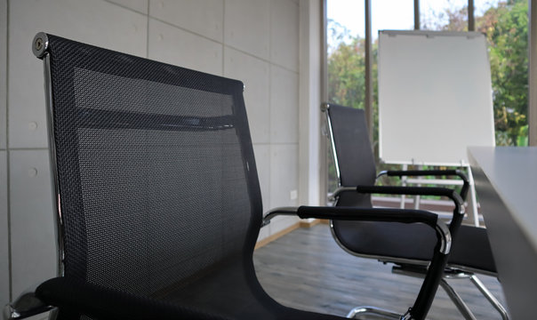 The picture of office with two black chairs and white table with white baord. The black ground of green trees. As an office for recruiting and interview the new applicants