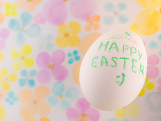 White chicken egg with a green text Happy Easter on floral paper