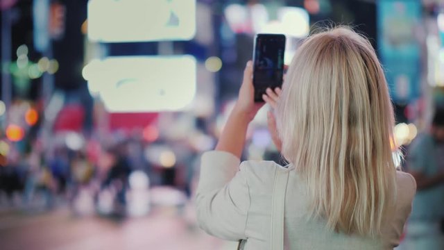 Tourist takes pictures with a smartphone on the famous Times Square in New York, rear view