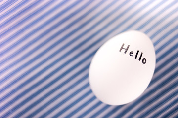 White chicken egg with black text Hello on the stripped blue background