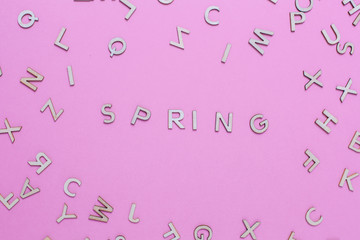Wooden ABC alphabet letters on pink background. Spring word written with wooden letters