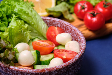 fresh vegetables and a bowl of salad with mozzarella on a blue background.  Caprese salad . Lettuce, cherry tomatoes, mozzarella, 