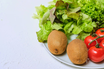 kiwis, lettuce and cherry tomatoes on a white plate on a white background