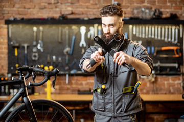 Portrait of a handsome bearded repairman in workwear standing with wrenches at the bicycle workshop