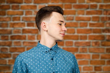 White young guy dressed in blue shirt on brick wall background smiles and looking aside