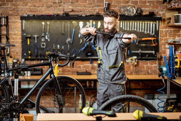 Plakat Portrait of a handsome bearded repairman in workwear standing with wrenches at the bicycle workshop