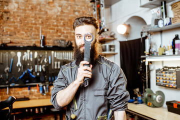 Portrait of a handsome bearded repairman in workwear standing with wrenches at the bicycle workshop