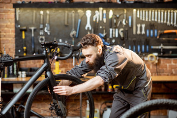 Obraz na płótnie Canvas Handsome bearded repairman in workwear serving a sports bike at the bicycle workshop