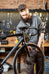 Fototapeta na wymiar Handsome bearded repairman in workwear serving a sports bike at the bicycle workshop