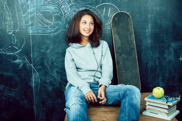 Fototapeta na wymiar young cute teenage girl in classroom at blackboard seating on table smiling, modern hipster concept
