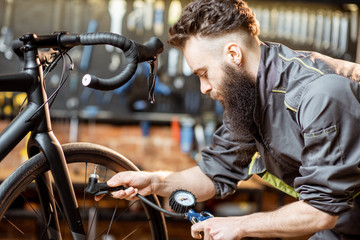 Repairman in workwear serving a sports bike, pumping wheels at the bicycle workshop