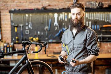 Fototapeta na wymiar Portrait of a handsome cheerful repairman in workwear at the bicycle workshop