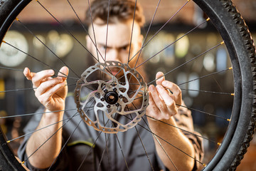Handsome bearded repairman in workwear holding bicycle wheel with disc breaks at the bicycle...