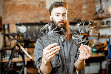 Portrait of a handsome bearded repairman in workwear with brake discs in the bicycle workshop