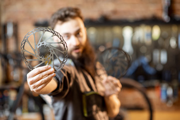 Fototapeta na wymiar Portrait of a handsome bearded repairman in workwear with brake discs in the bicycle workshop