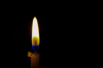 A burning candle on black background, close up.