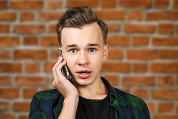 portrait of scared White young guy writes a message on the mobile phone and smiles. Man on brick wall background