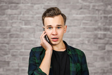 portrait of scared White young guy writes a message on the mobile phone and smiles. Man on brick wall background
