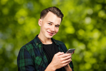 Fototapeta na wymiar White young guy writes a message on the mobile phone and smiles. Man on green bokeh background