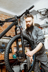 Fototapeta na wymiar Handsome bearded repairman in workwear mounting wheel on a mountain bicycle at the workshop