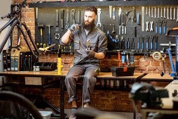 Portrait of a handsome repairman in workwear sitting with wrenches and different work tools at the bicycle workshop - Powered by Adobe