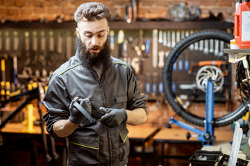 Fototapeta na wymiar Handsome bearded repairman in workwear working in the beautiful bicycle workshop