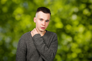 Portrait of white yong guy in gray sweater and short haircut, on green bokeh background