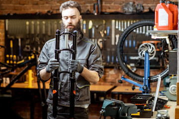 Fototapeta na wymiar Handsome repairman holding bicycle fork while working in the beautiful bicycle workshop