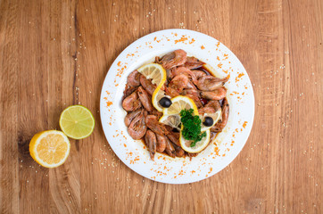 Appetizing shrimps in soy sauce on a white dish. Shrimps with olives and lemon. Restaurant seafood...