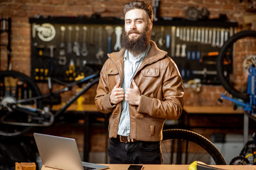 Portrait of a handsome bearded man as bicycle store owner or manager standing with laptop at the bicycle workshop