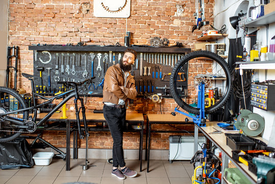 Portrait of a young stylish businessman as a shop owner standing at the bicycle workshop