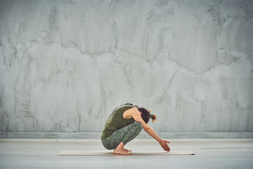 Young Caucasian woman squatting on mat and doing Garland yoga posture.