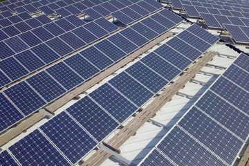 Solar panels spread across an industrial roof - Aerial image.