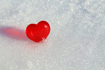 Red glass heart in the snow. Close-up. Background. Texture.