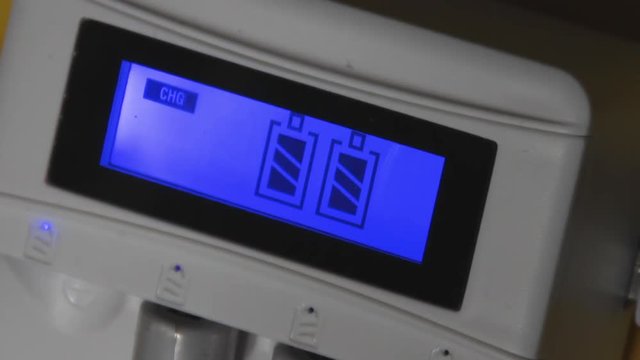 LCD display shows progress of refilling of rechargeable NiMh batteries in universal multi type battery charger device. Metal hydride accumulators AAA size. Green technology for environment protection