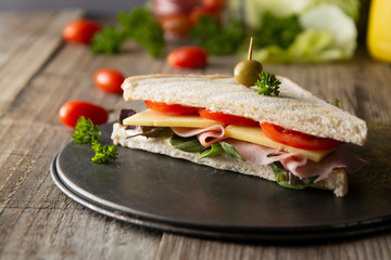 Homemade club sandwich. Toasted white bread triangles with ham, cheese fresh vegetables. Wooden table.