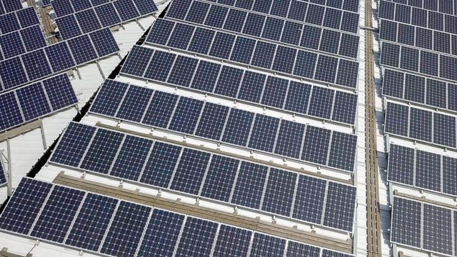 Solar panels spread across an industrial roof - Aerial image.
