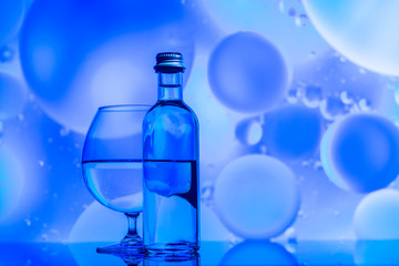 transparent glass and bottle with water and oily drops on azure background 