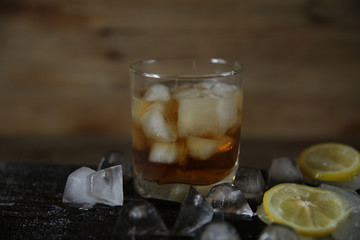 Glass of whiskey with ice on a wooden oak background with ice and lemon