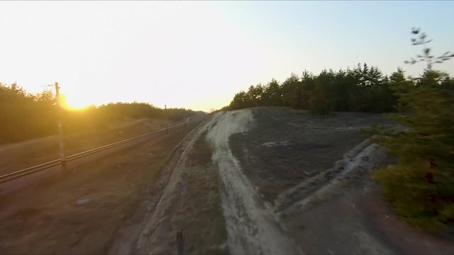 Drone racing view. Fly over dust road in forest at sunset. Dynamic shot