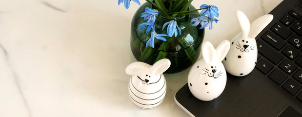 Easter concept banner. Flat lay office table, workspace with laptop, Easter bunny, bouquet blue spring flowers, notebook on marble background.