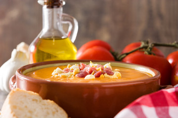 Typical Spanish salmorejo cream with ham and egg on wooden table.