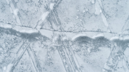 Naklejka na ściany i meble Frozen water surface. Ice on a lake. Cracked on ice. Cracked on the surface of a frozen lake. Snow on ice. The texture of the frozen surface of the water.