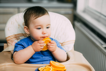 a little girl in a blue t-shirt and a blue plate sitting in a child's chair eating an orange